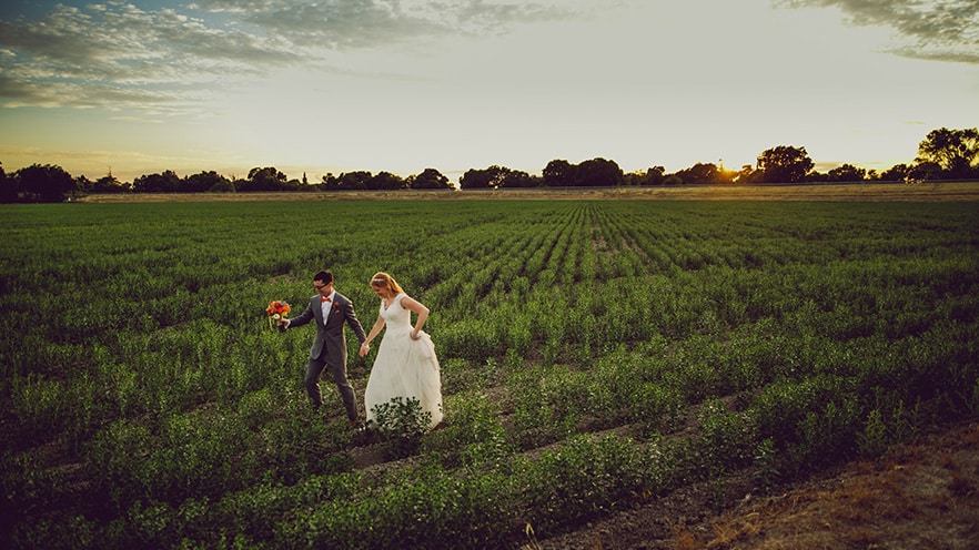 Candid shot of bride and groom walking through the field at sunset.