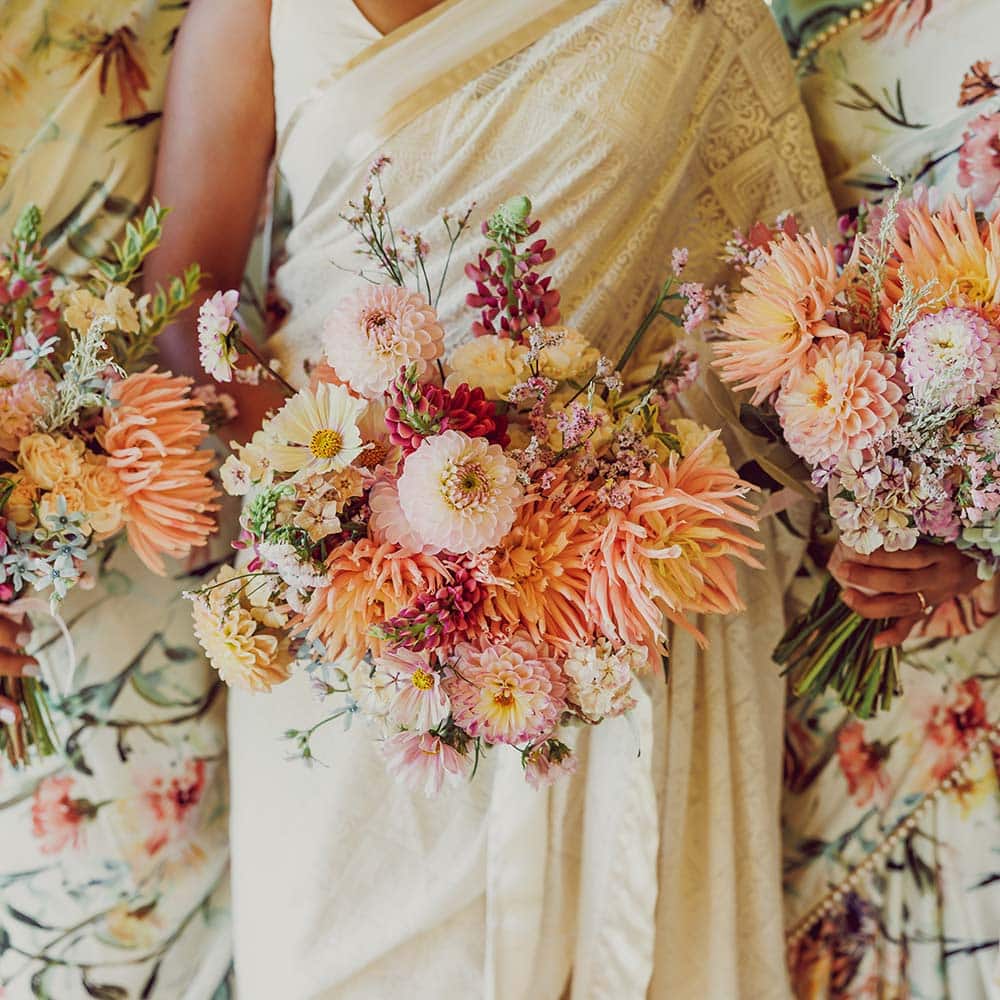 An up close photo of the bride and a bridesmaid on each side of her with them holding orange and yellow bouquets.