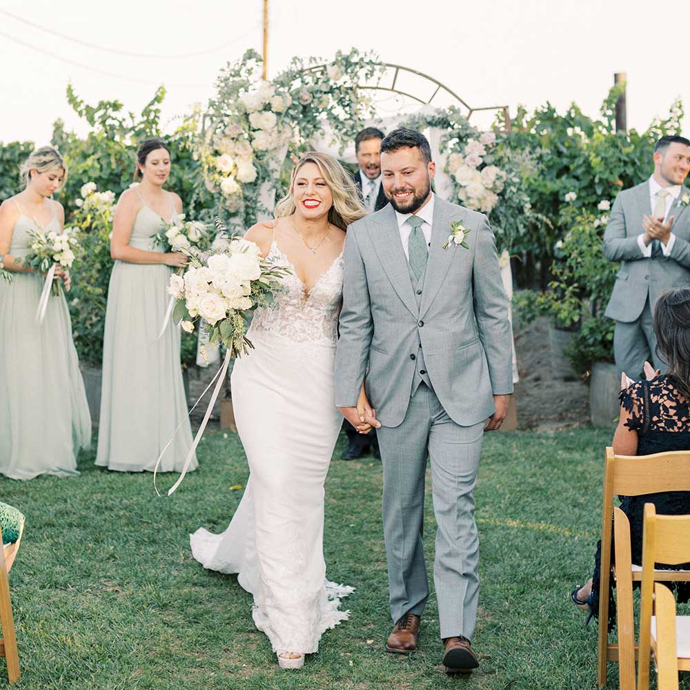 A bride and groom hold hands and smile as they walk back down the aisle after saying their I do's.