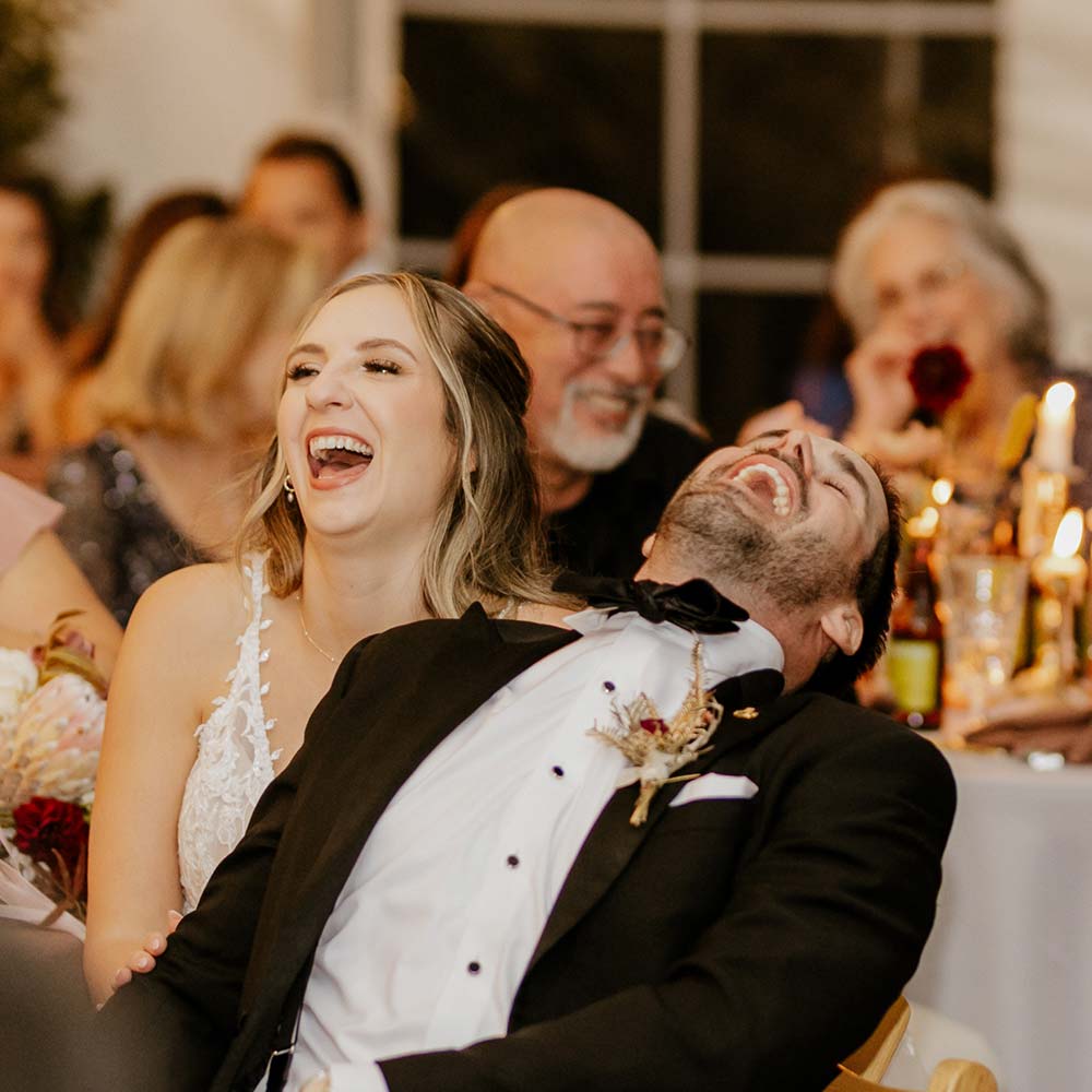 The bride and groom share laughs as they are surrounded by their guests under the covered tent.