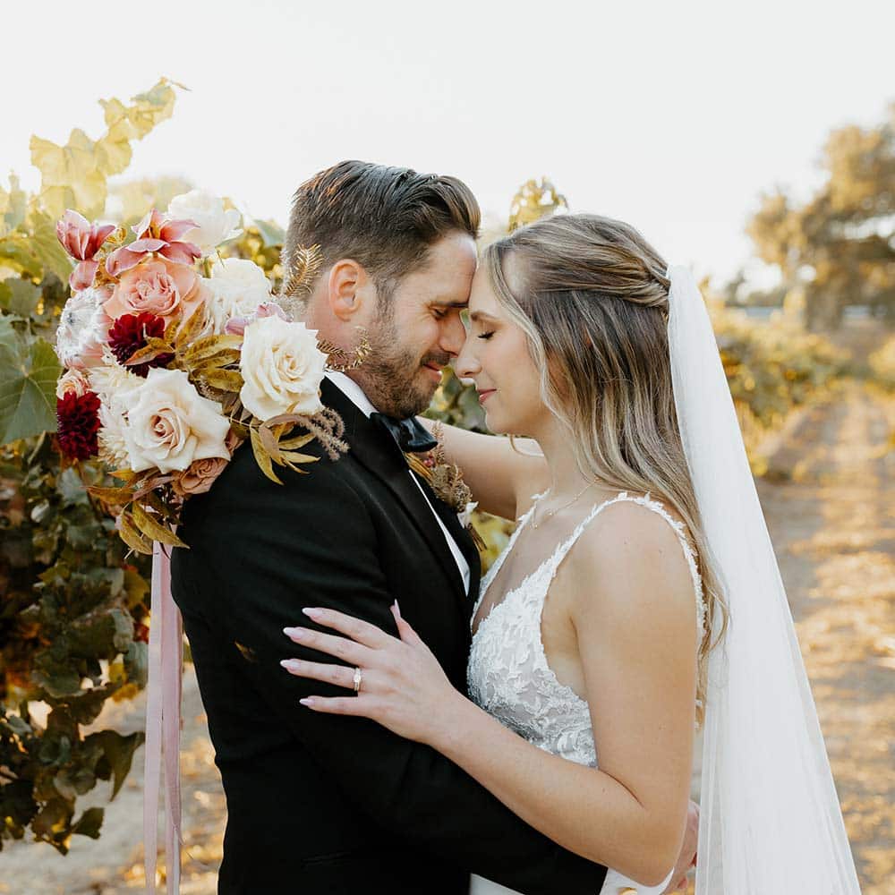 The bride and groom embrace with their eyes closed and surrounded by vineyards.