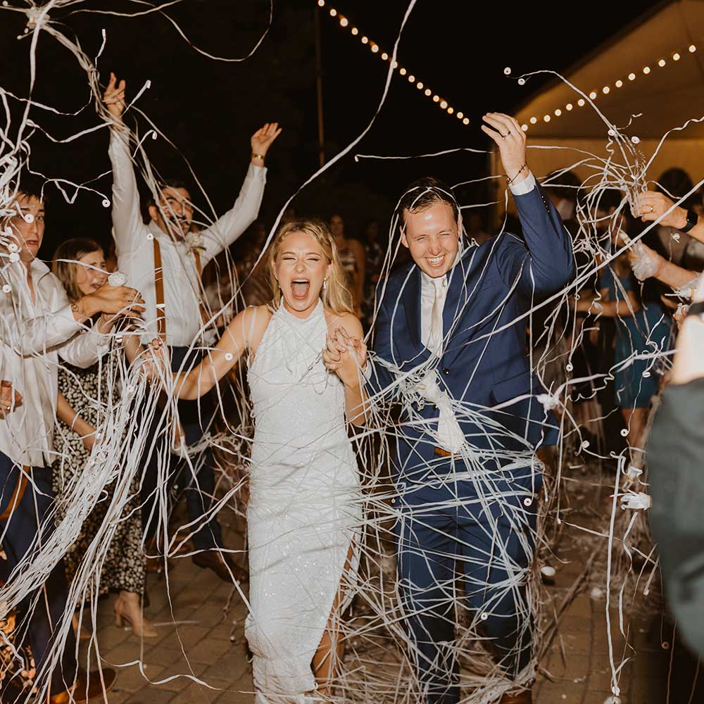 The bride and groom walk through an explosion of confettis as their guests cheer them on at their outdoor wedding in Sacramento.