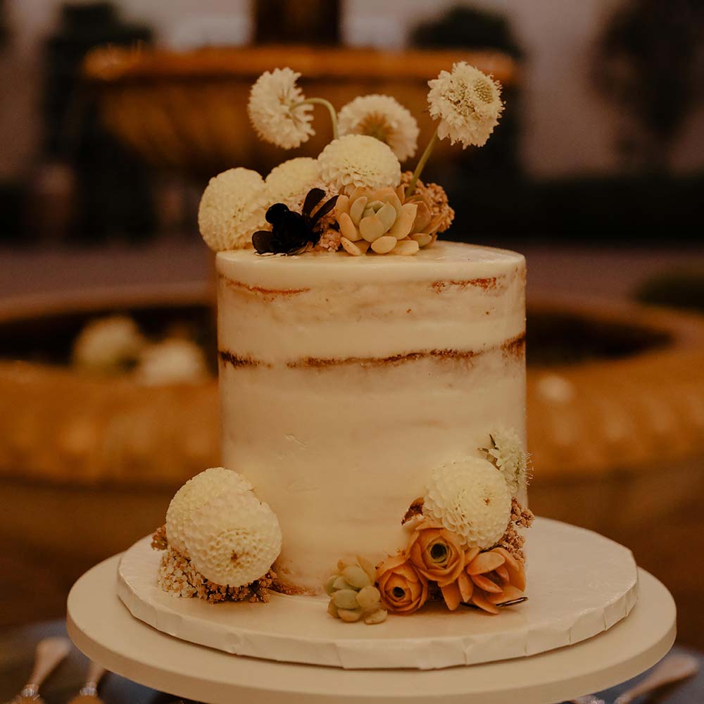 The one layer cake with rustic white and orange flowers and succulents on top and on the bottom with the 3-tiered fountain and winery in the background.