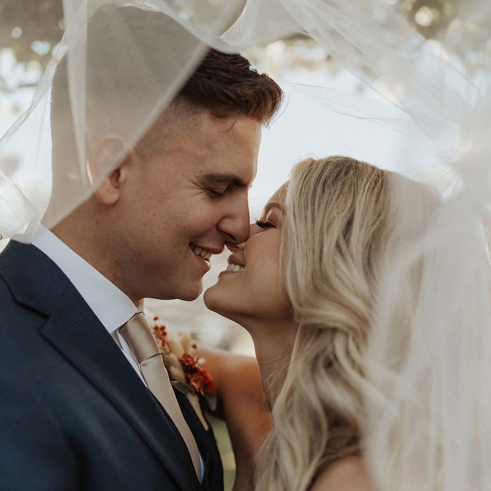 The bride and groom share a kiss as they are partially hidden under her veil.