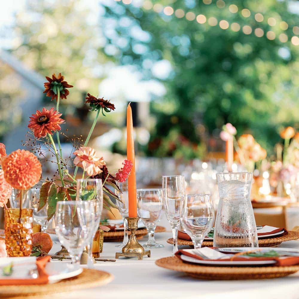 A colorful place setting complete with rust orange and green colors throughout as the market lights from the covered tent and winery are faded in the background at this winery wedding in Sacramento.