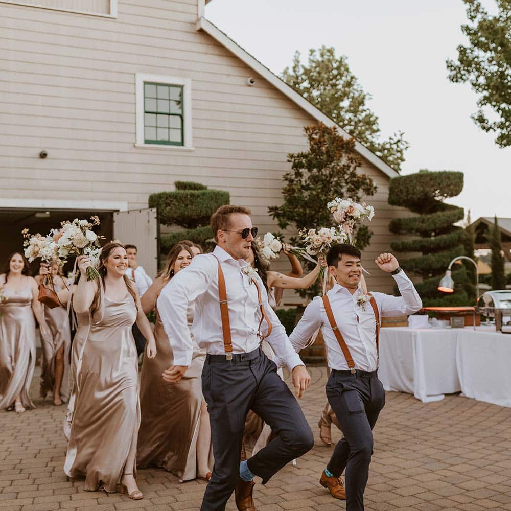 The groomsman and brides coming out of the double doors of the winery dancing and with smiles on their faces as the move toward the guests at this outdoor winery wedding in Sacramento.