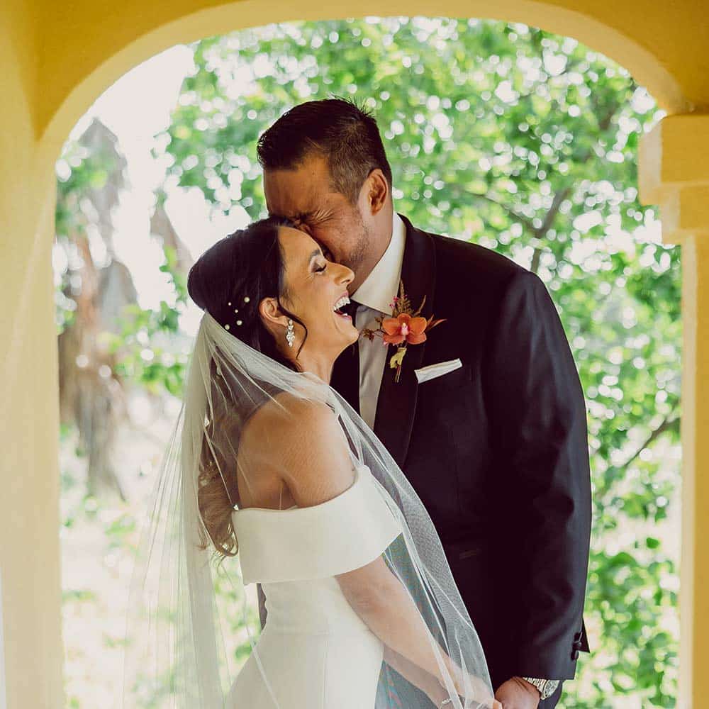 The groom holds the brides hand and leans into her as he cries seeing her for the first time and she holds onto him and smiles.