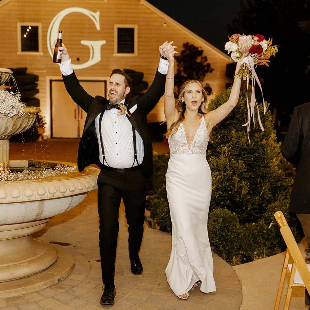 The bride and groom raise their hands and pass the three tiered foundation which is full of baby's breath as they make their way to their guests.