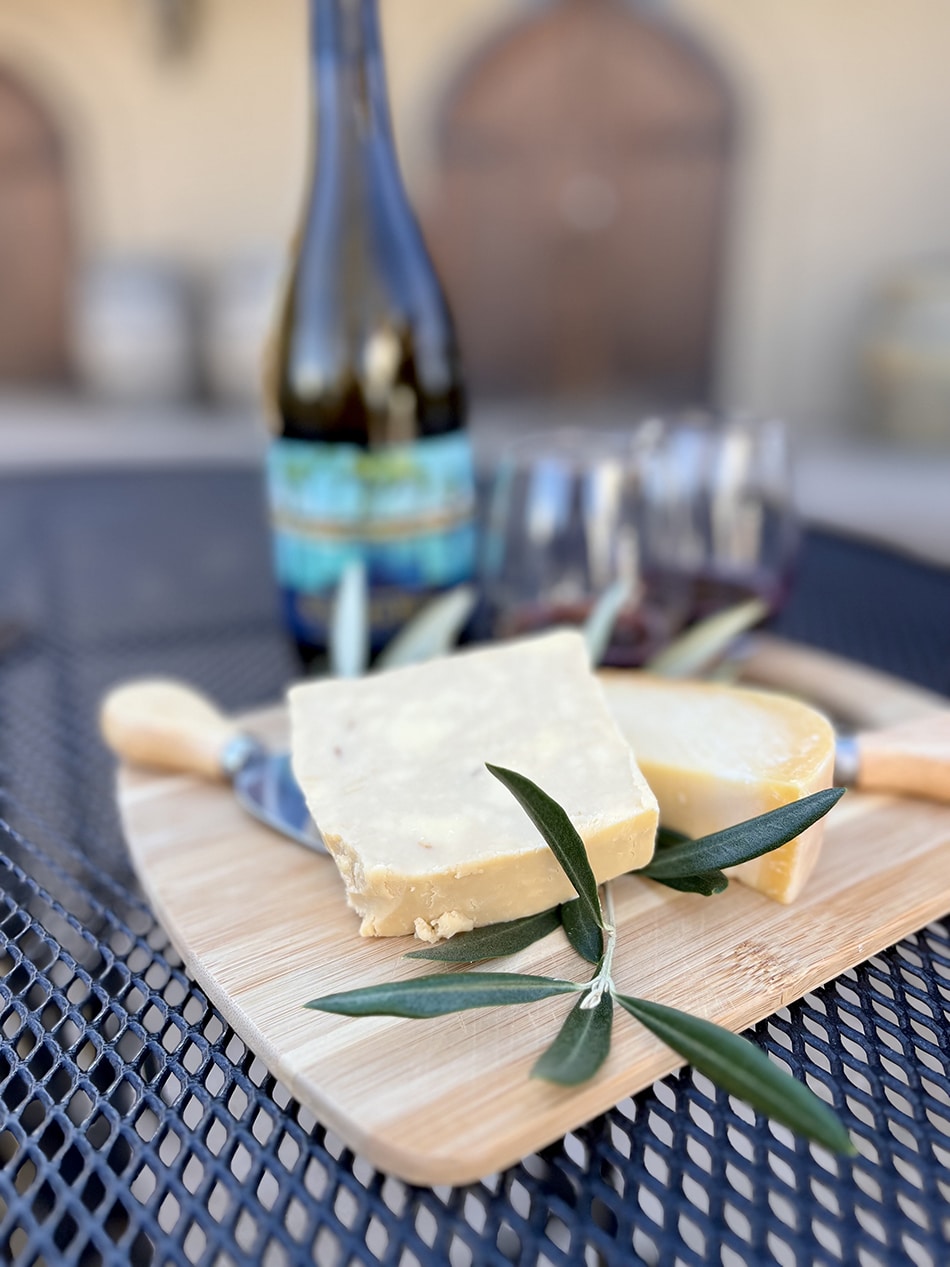 Cheese is displayed on a cutting board in front of a bottle of Scribner Bend Syrah.