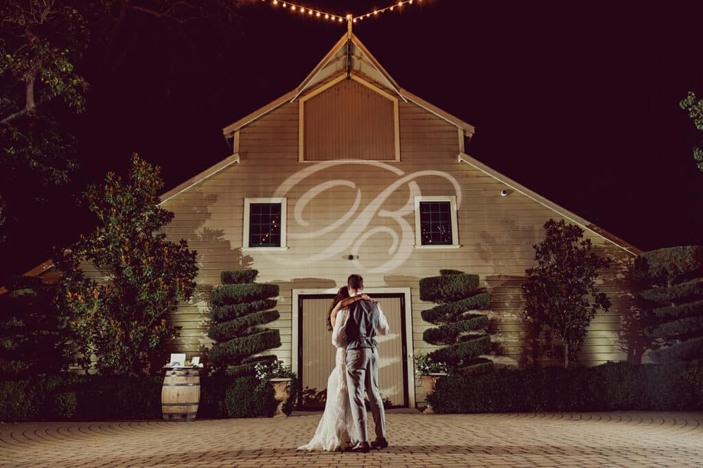 Bride and Groom dance under night sky in front of barn and gardens at their outdoor wedding.