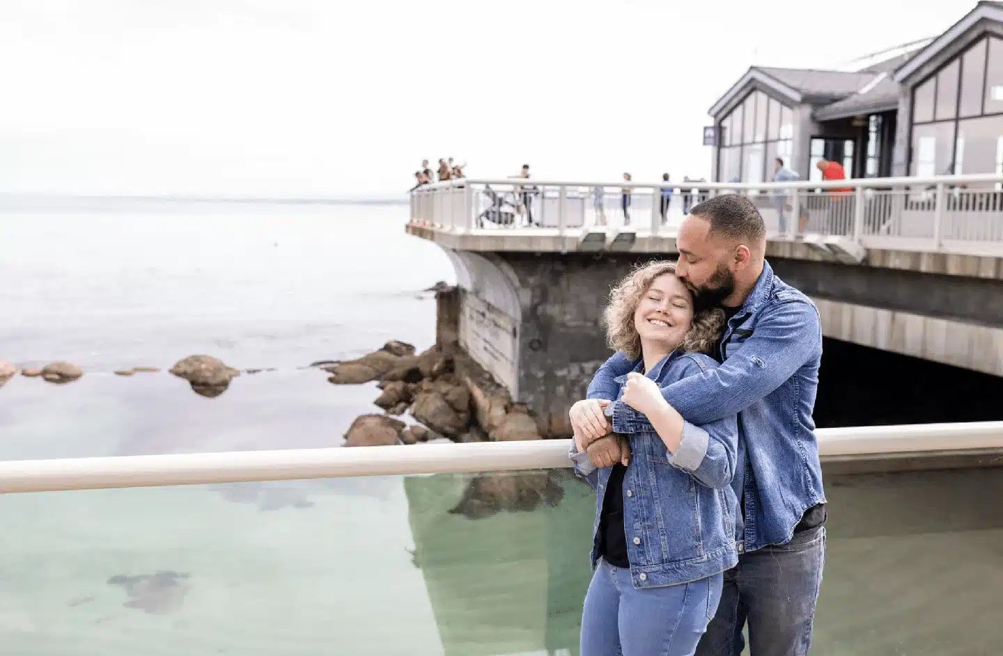 Engaged Couple Oceanside engaged couple standing against an oceanside rail in front of an observation point. Man standing behind the girl kissing her forehead